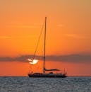 A sailboat glides across the sea against a vibrant sunset near the Balearic Islands.